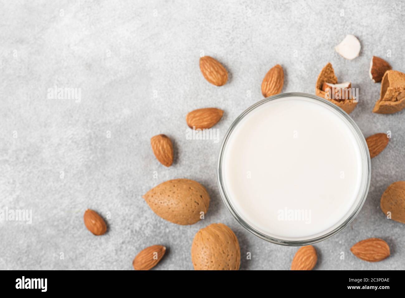 Mandelmilch in einem Glas mit Mandelnüssen auf Betongrund. Vegane milchfreie Pflanzenmilch. Draufsicht. Nahaufnahme Stockfoto