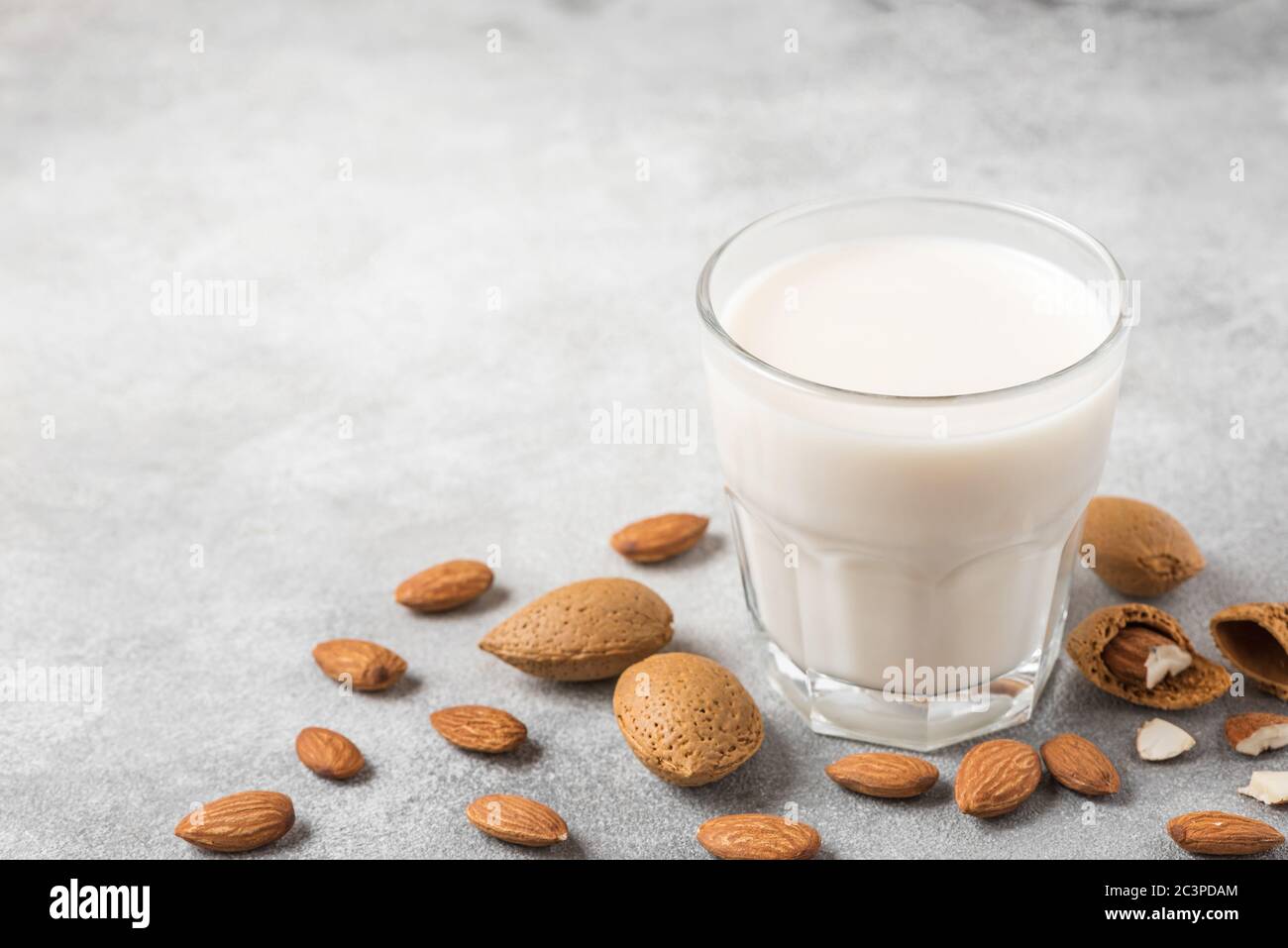 Mandelmilch in einem Glas mit Mandelnüssen auf Betongrund. Vegane milchfreie Pflanzenmilch. Nahaufnahme Stockfoto