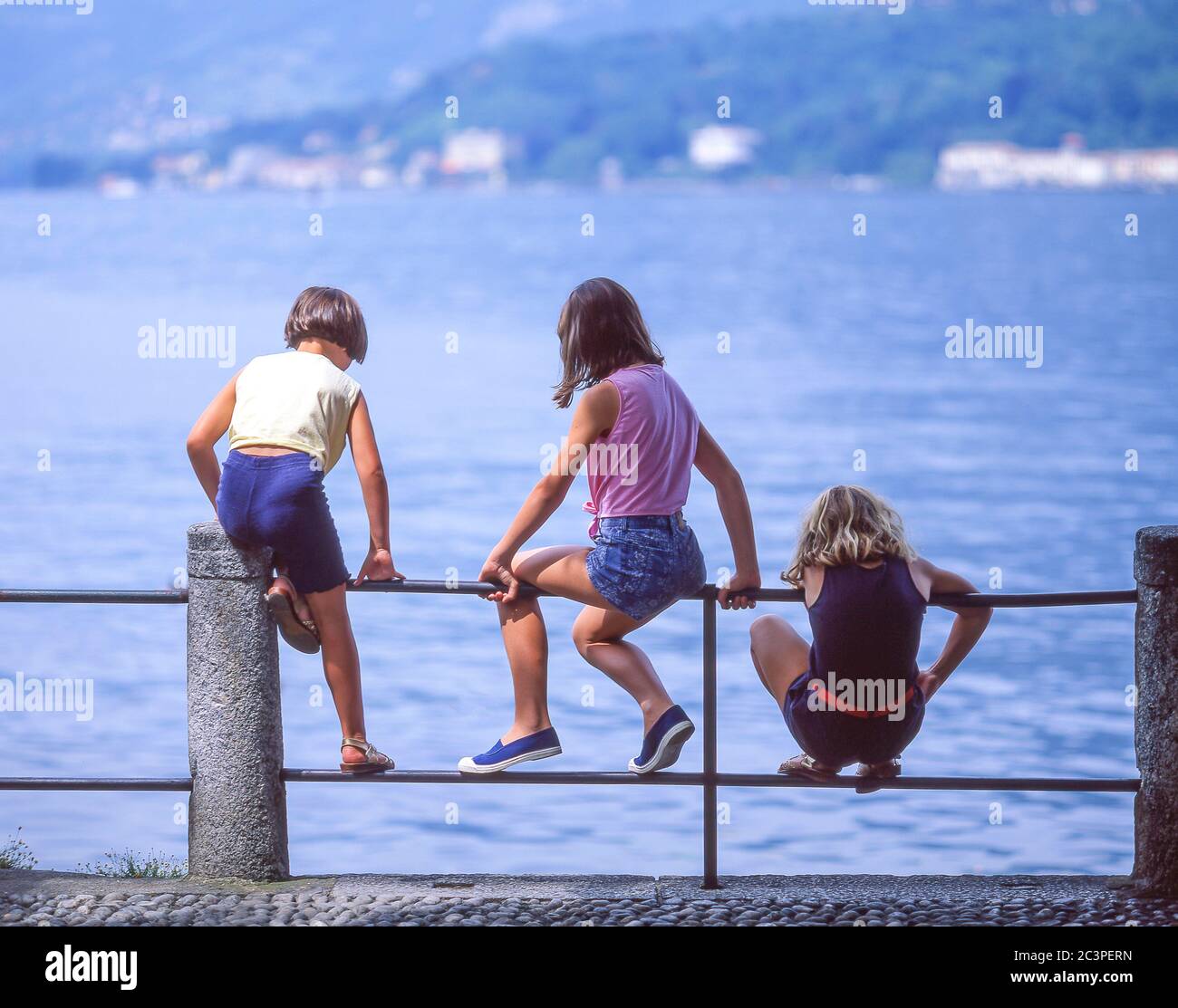 Lokale Kinder sitzen auf Geländer am Ufer des Comer Sees, Tremezzo, Provinz Como, Lombardei Region, Italien Stockfoto
