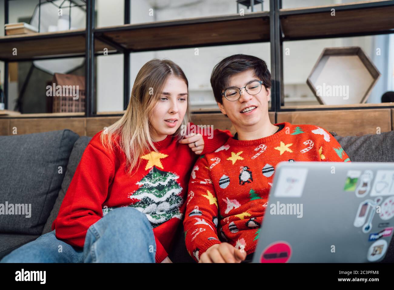 Glückliches Paar mit Laptop zusammen auf dem Sofa, lächelndes junges Mädchen und Kerl, die Spaß haben, zu Hause zu sprechen Stockfoto