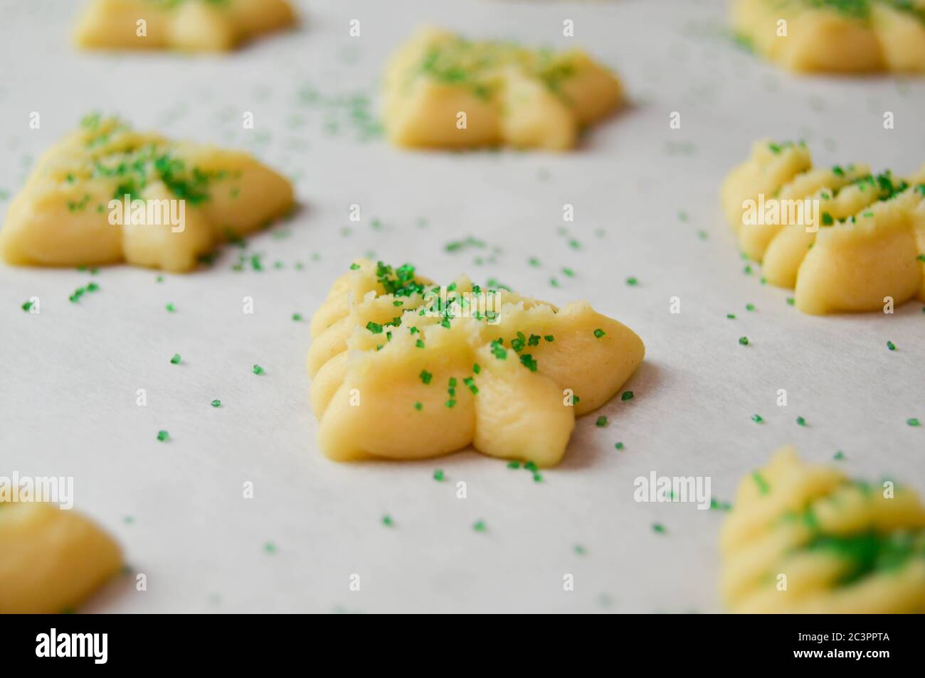 spritz Kekse in weihnachtsbaumformen auf Pergamentpapier mit grünen Zuckerstreuseln Stockfoto