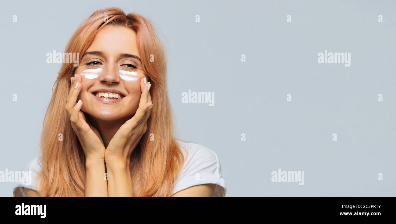 Portrait der jungen fröhlichen niedlichen Frau lächeln und Anwendung Sonnencreme (Sonnencreme) auf das Gesicht. Hübsches weibliches verschmiertes Gesicht, Wangen mit Sonnenschutz Stockfoto