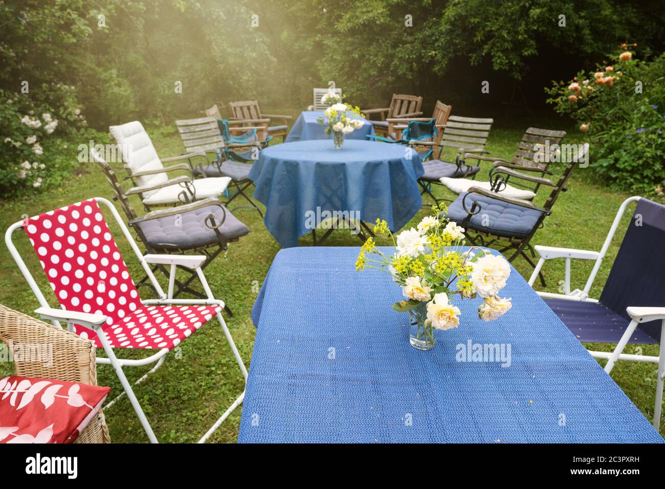 Informelle Gartenparty mit Tischen, blauen Tischdecken und verschiedenen Stühlen in einem ländlichen Hinterhof, ausgewählte Fokus eingerichtet Stockfoto