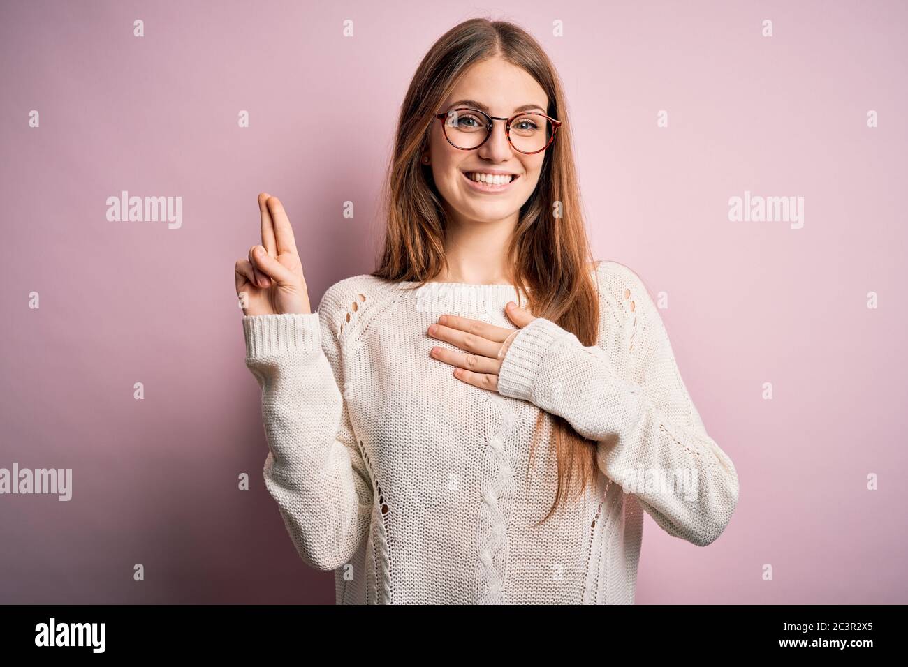 Junge schöne Rothaarige Frau trägt lässige Pullover und Brille über rosa Hintergrund lächelnd Fluchen mit der Hand auf Brust und Finger nach oben, so dass ein loy Stockfoto
