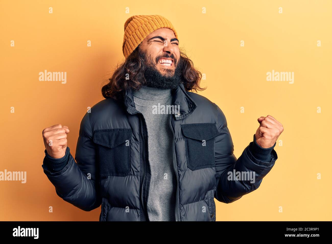 Junger arabischer Mann trägt lässige Winterkleidung sehr glücklich und aufgeregt tun Sieger Geste mit den Armen angehoben, lächelnd und schreien nach Erfolg. Celebrat Stockfoto