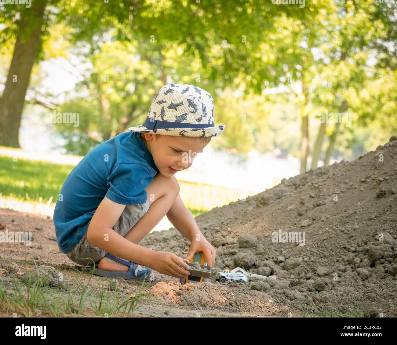 Kleines Kind spielt an einem sonnigen Sommertag mit einem Spielzeugbaufahrzeug auf einem großen Sandhaufen. Stockfoto