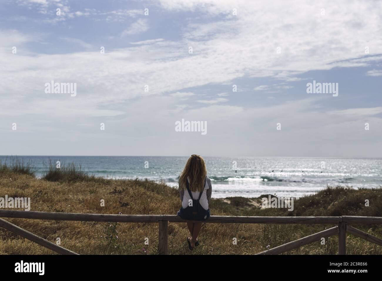 Junge Frau sitzt auf einem Holzzaun von der umgeben Meer unter dem Sonnenlicht und einem bewölkten Himmel Stockfoto