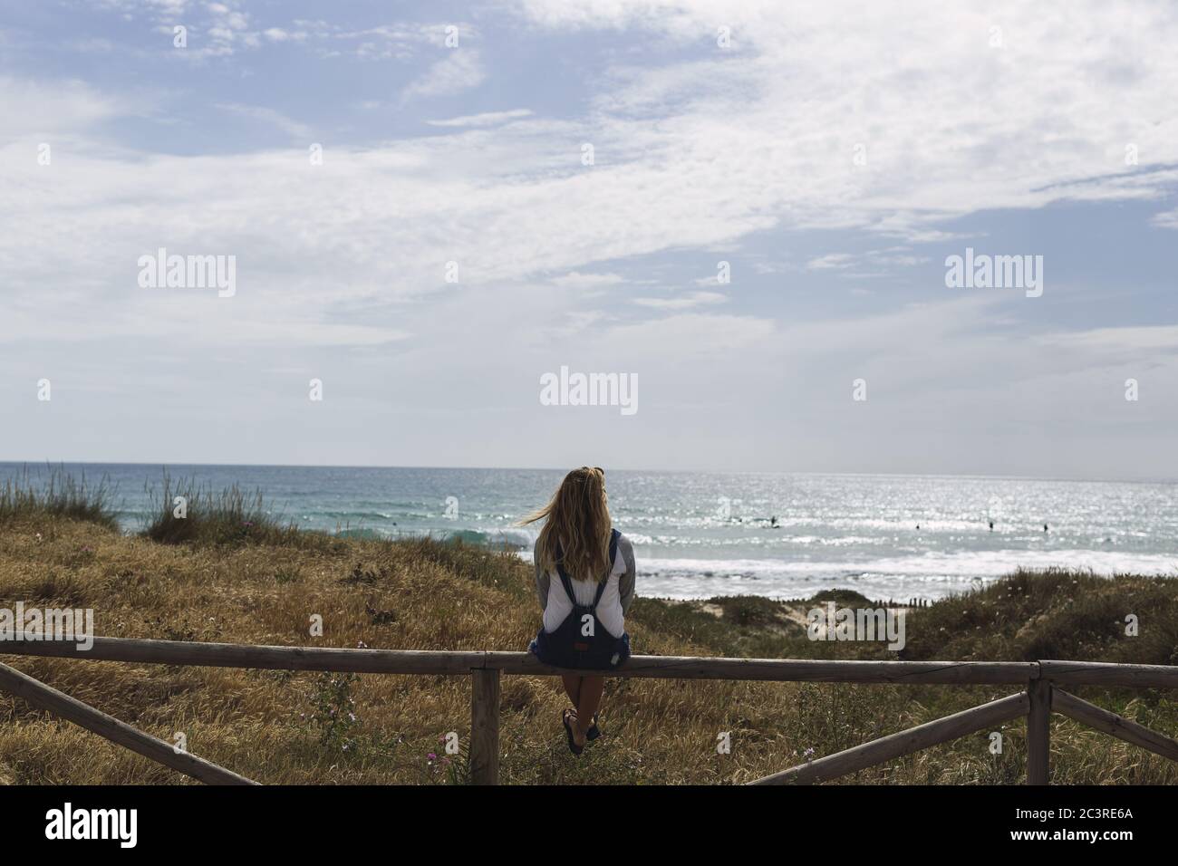 Junge Frau sitzt auf einem Holzzaun von der umgeben Meer unter dem Sonnenlicht und einem bewölkten Himmel Stockfoto