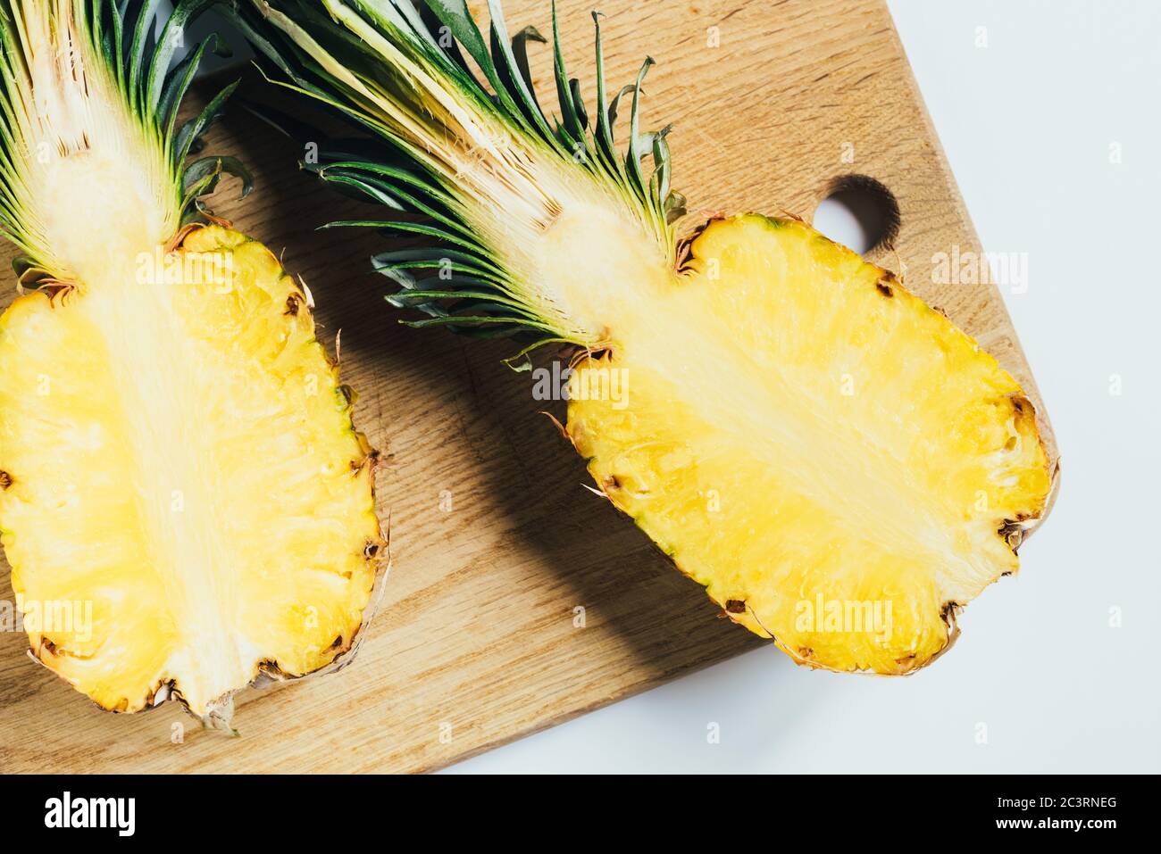 Draufsicht auf saftige Ananas Hälften auf Holz Schneidebrett auf weißem Hintergrund Stockfoto