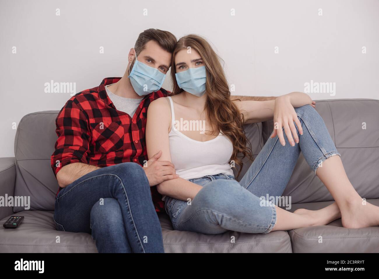 Deprimiert junges Paar in medizinischen Masken sitzen auf dem Sofa und Blick auf die Kamera Stockfoto