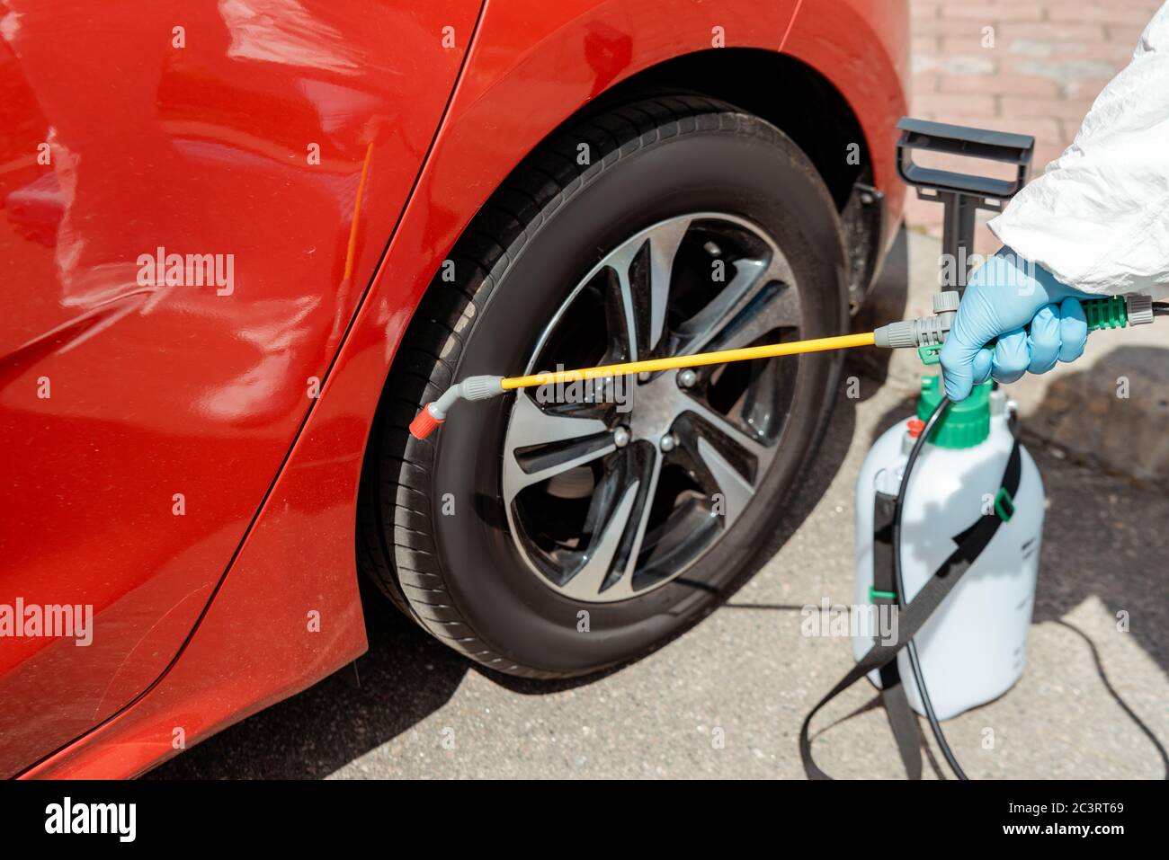 Beschnittene Ansicht des Spezialisten in Schutzanzug Reinigung Auto mit Desinfektionsmittel in Sprühbeutel während covid-19 Pandemie Stockfoto
