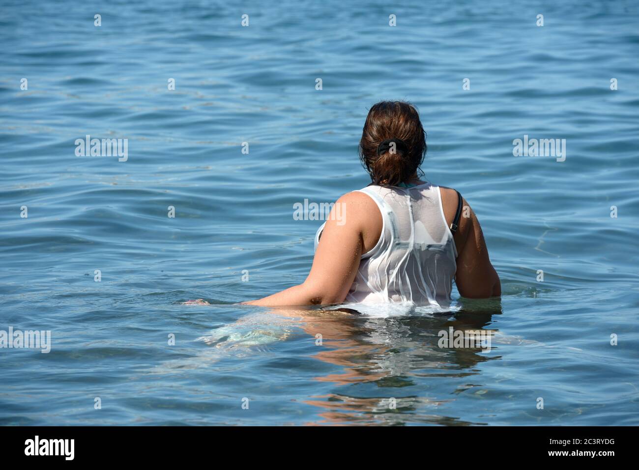 Nahaufnahme von der Rückseite der Frau mit dunklem Haar, das in ruhigen Ozean blauem Wasser steht. Stockfoto