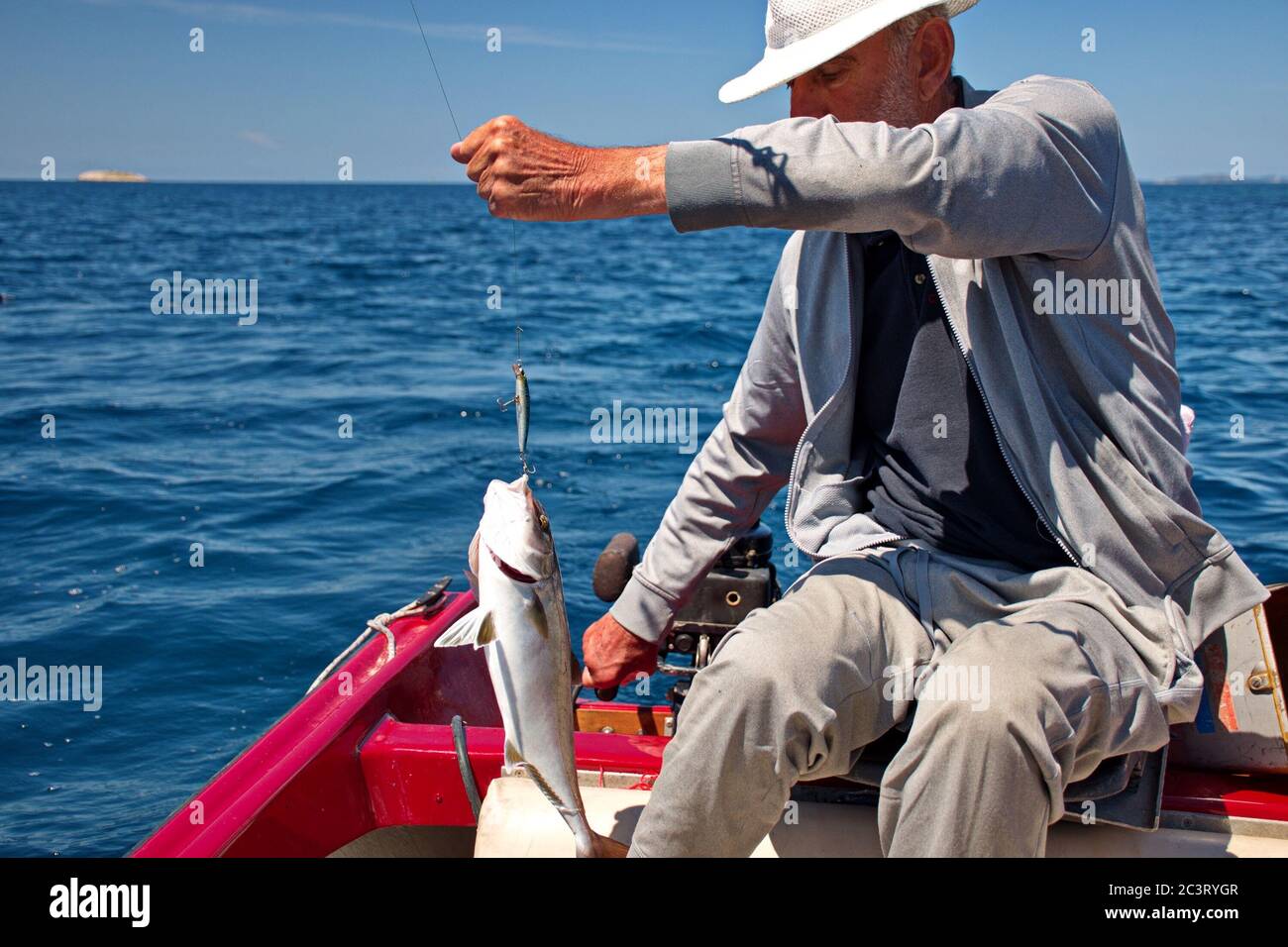 Alter Fischer, der in einem Boot sitzt und Fisch am Haken hält Stockfoto