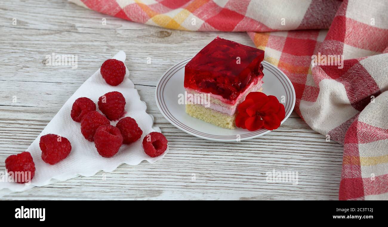 Stück Himbeerkuchen Dessert auf dekorativen weißen Teller mit roter Blume, neben frischen Himbeeren, Küchentücher, auf Holztisch close up. Stockfoto