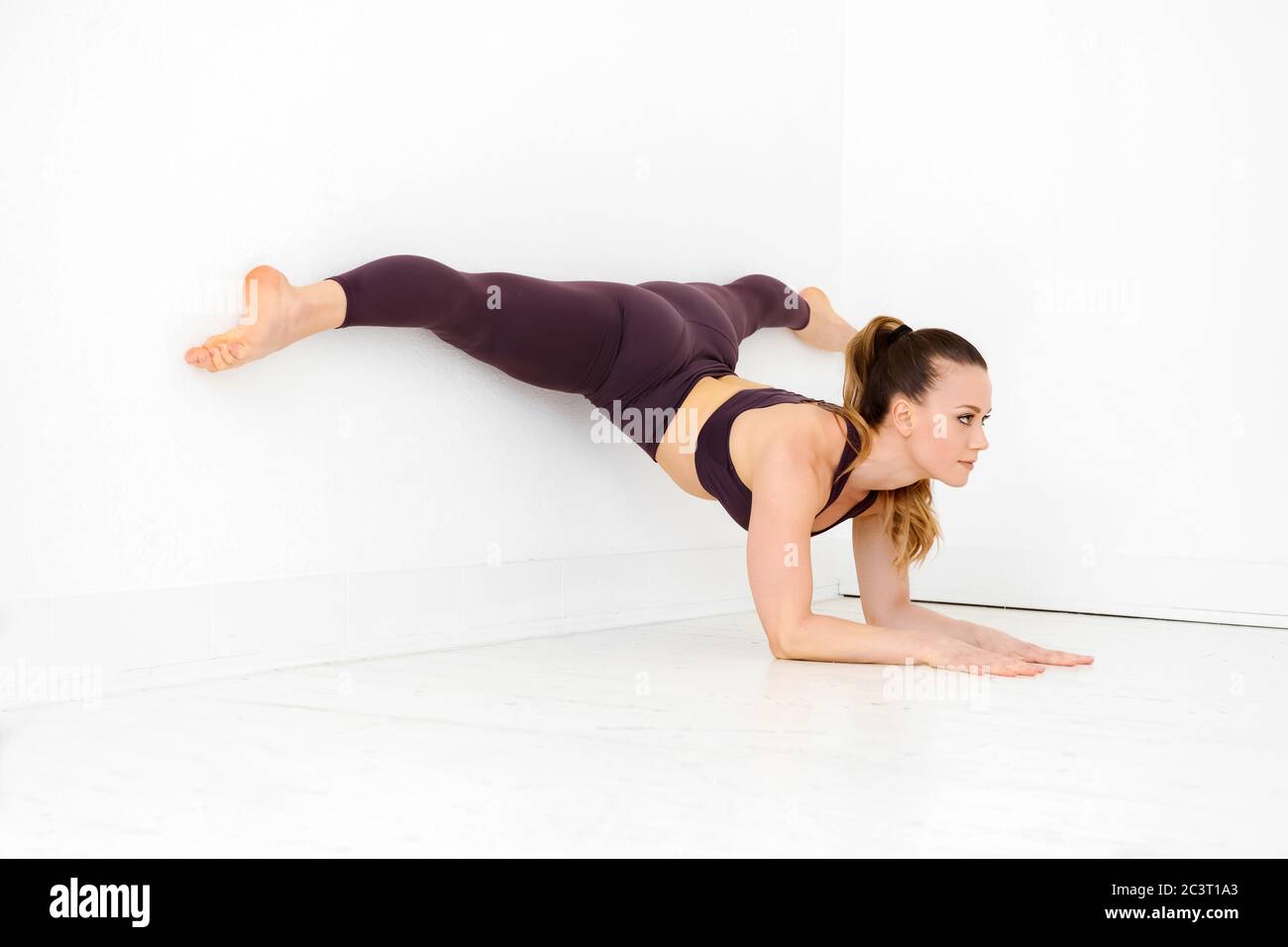 Frau Athlet tun eine Ellbogenwand Split Yoga Pose in der Ecke eines High-Key-weißen Turnhalle in einem aktiven Lebensstil oder Gesundheit und Fitness-Konzept Stockfoto