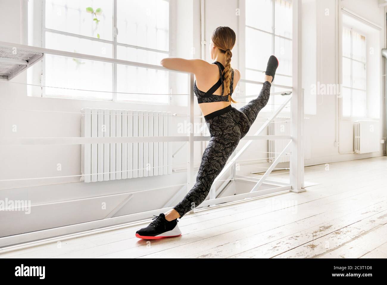 Frau, die eine frontale geteilte Yoga-Pose mit einer Bar in einer Rückansicht zeigt getönte Muskeln in einem High-Key-Fitnessstudio in einem Gesundheits-und Fitness-Konzept mit Copyspac Stockfoto