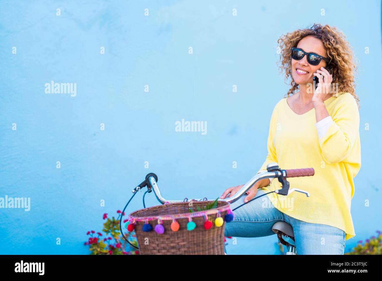 Schöne mittlere Alter gesunde junge Frau tun einen Anruf Setzen Sie sich auf einem Vintage farbigen Happy Bike und blauen Hintergrund Wand - Farben und glückliche Menschen Stockfoto