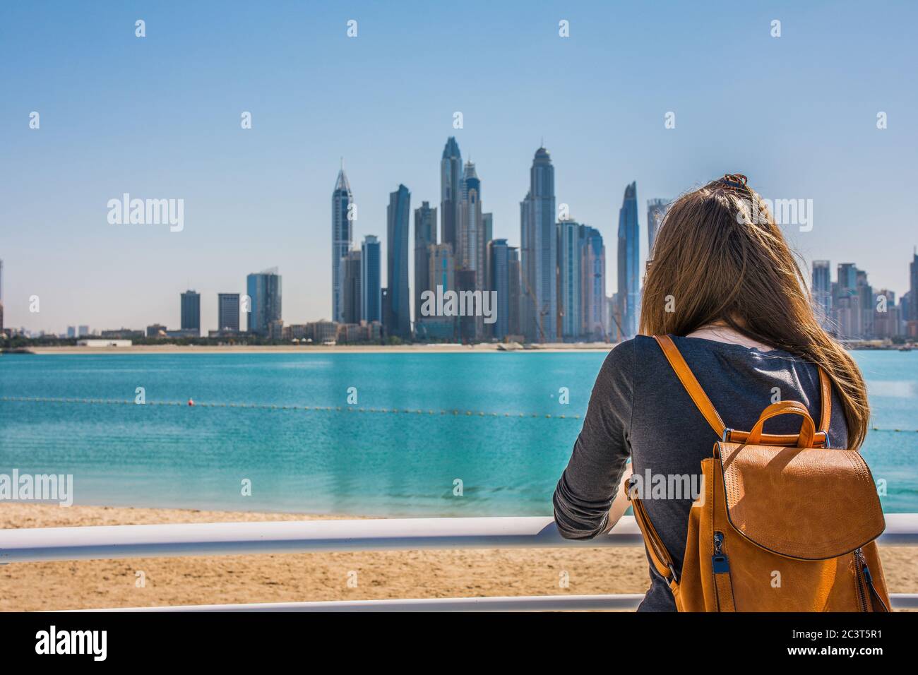 Junge Frau, die an einem sonnigen Tag vom Strand von Palm Jumeirah aus die Dubai Marina anschaut, Dubai, Vereinigte Arabische Emirate Stockfoto