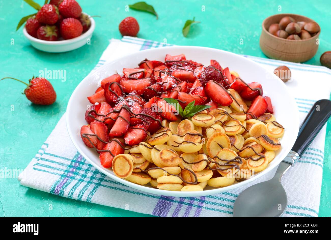 Pfannkuchen Müsli in einer Schüssel mit frischen Erdbeeren und Nüssen auf einem hellen Hintergrund. Leckeres und trendiges Frühstück. Bio-Holländische Mini-Pfannkuchen. Lebensmitteltrend Stockfoto