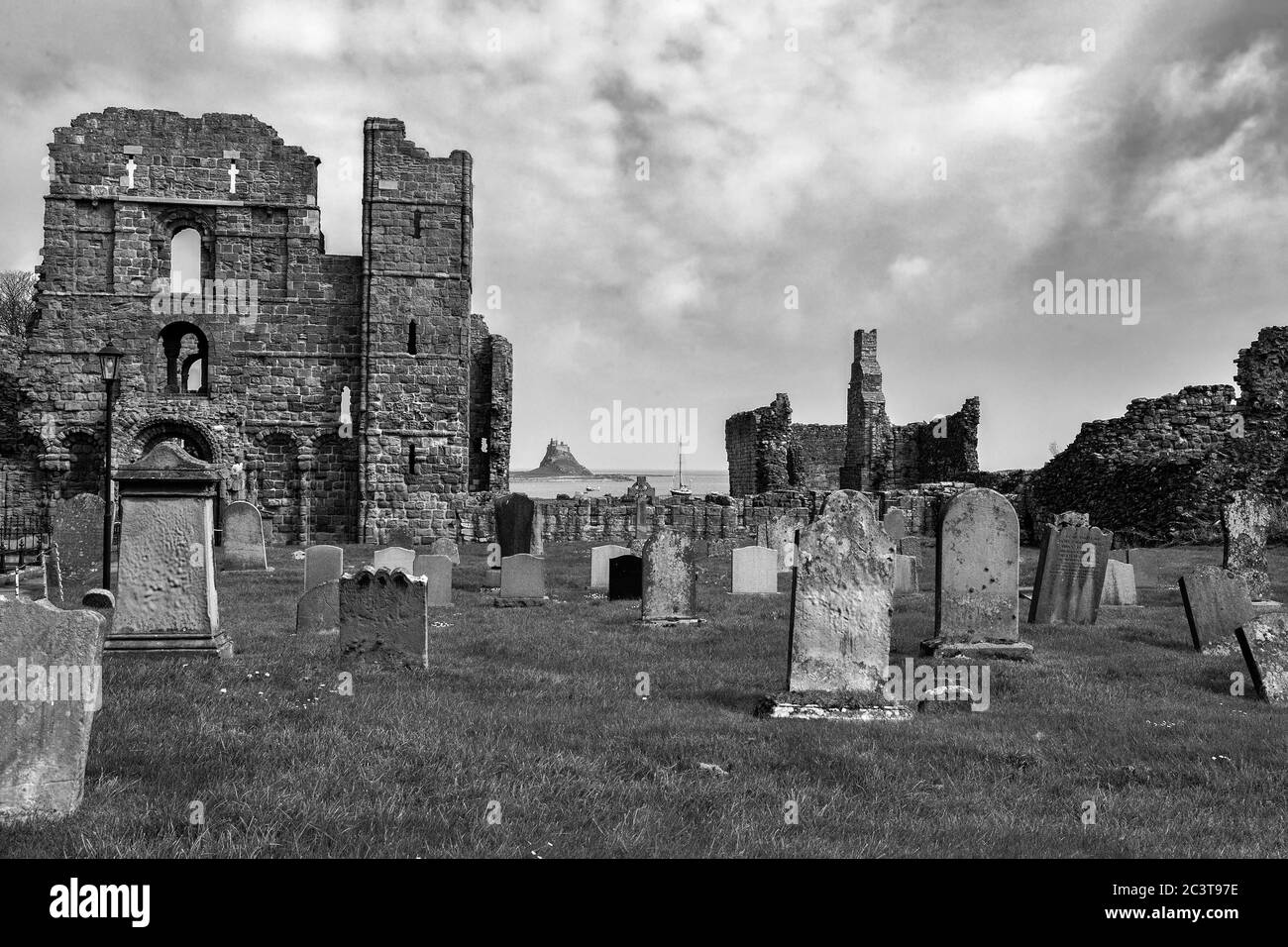 Friedhof, die Ruinen von Lundisfarne Priory und in der Ferne, Schloss Lundisfarne, Holy Island, Northumberland, England, Großbritannien. Schwarz-Weiß-Version Stockfoto