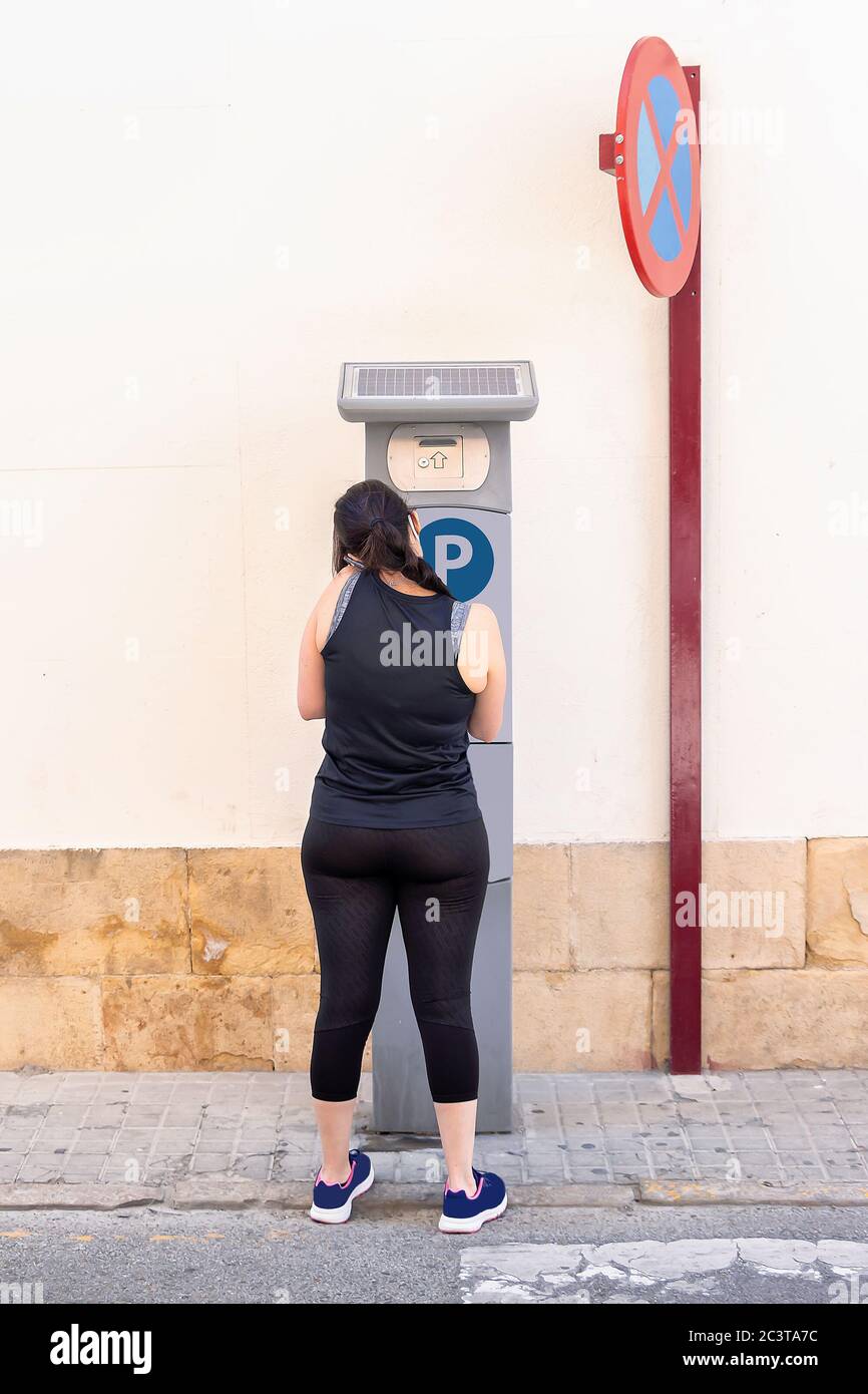 Rückansicht einer unbekannten Frau, die den Parkplatz auf der Straßenseite benutzt, während sie das Mobiltelefon benutzt Stockfoto