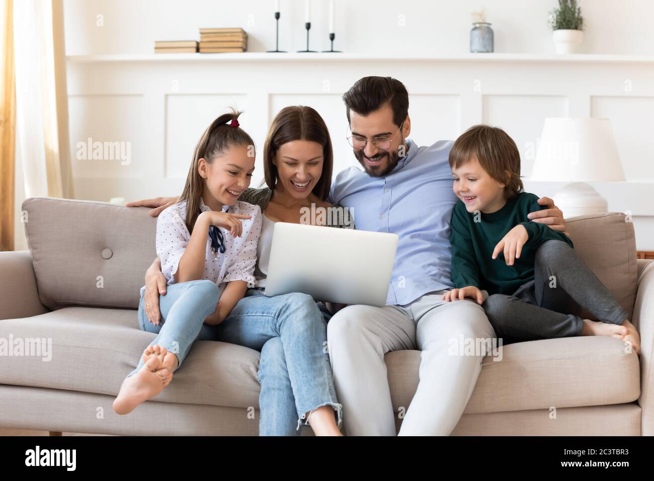 Glückliche Familie mit Kindern, die sich auf der Couch mit Laptop entspannen Stockfoto