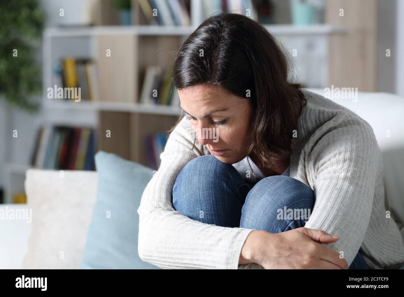 Nachdenkliche traurige Erwachsene Frau, die auf dem Sofa im Wohnzimmer zu Hause sitzt Stockfoto