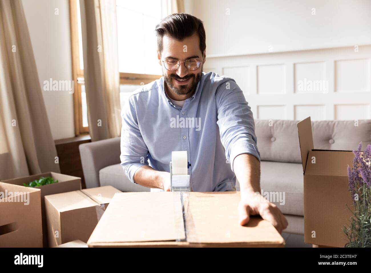 Lächelnder Mann trägt Brille Verpackung Karton mit Klebeband Stockfoto