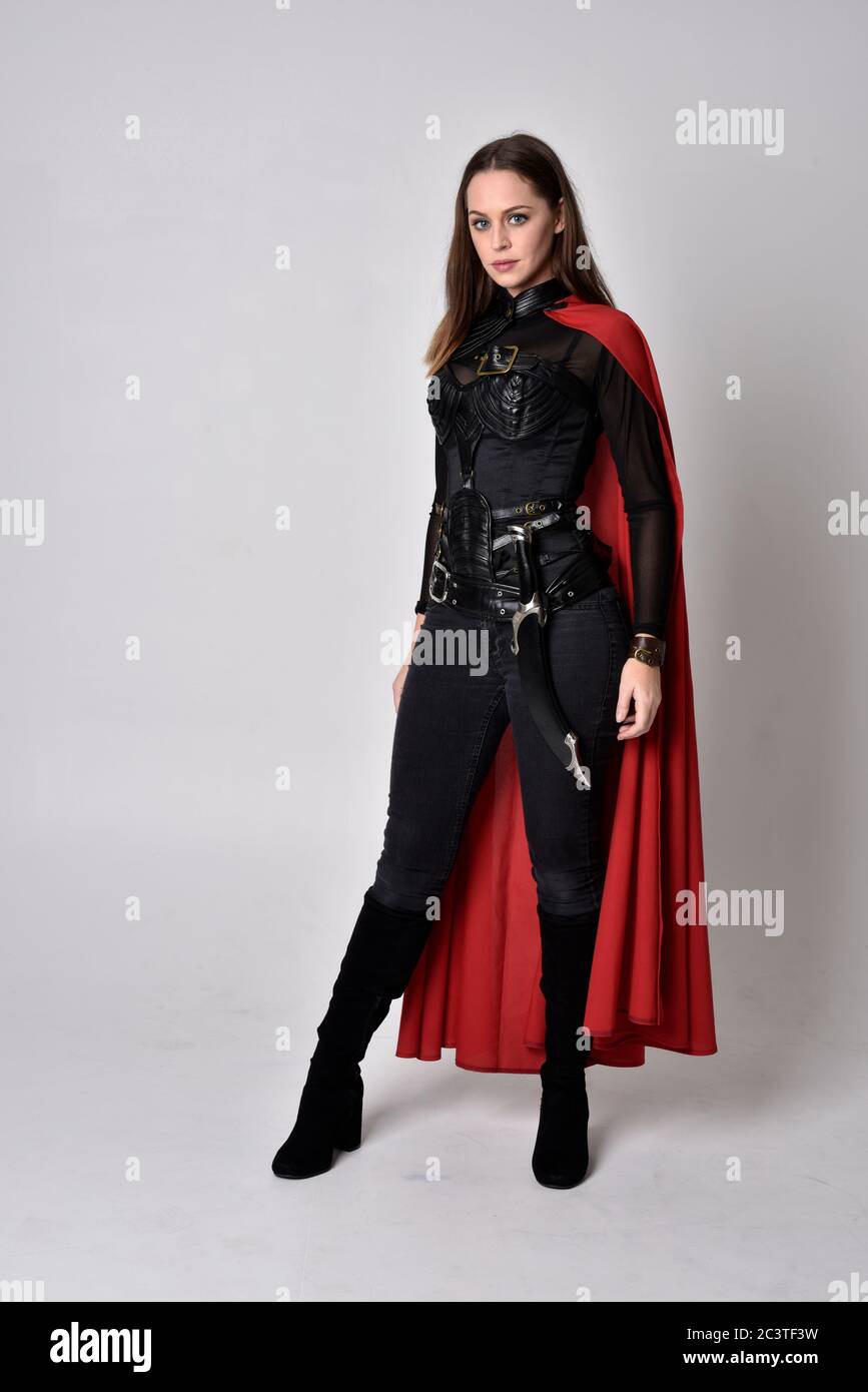 Portrait von Brünette Mädchen trägt schwarzen Leder Catsuit & roten Umhang.  In voller Länge stehende Pose, isoliert vor einem Studio-Hintergrund  Stockfotografie - Alamy