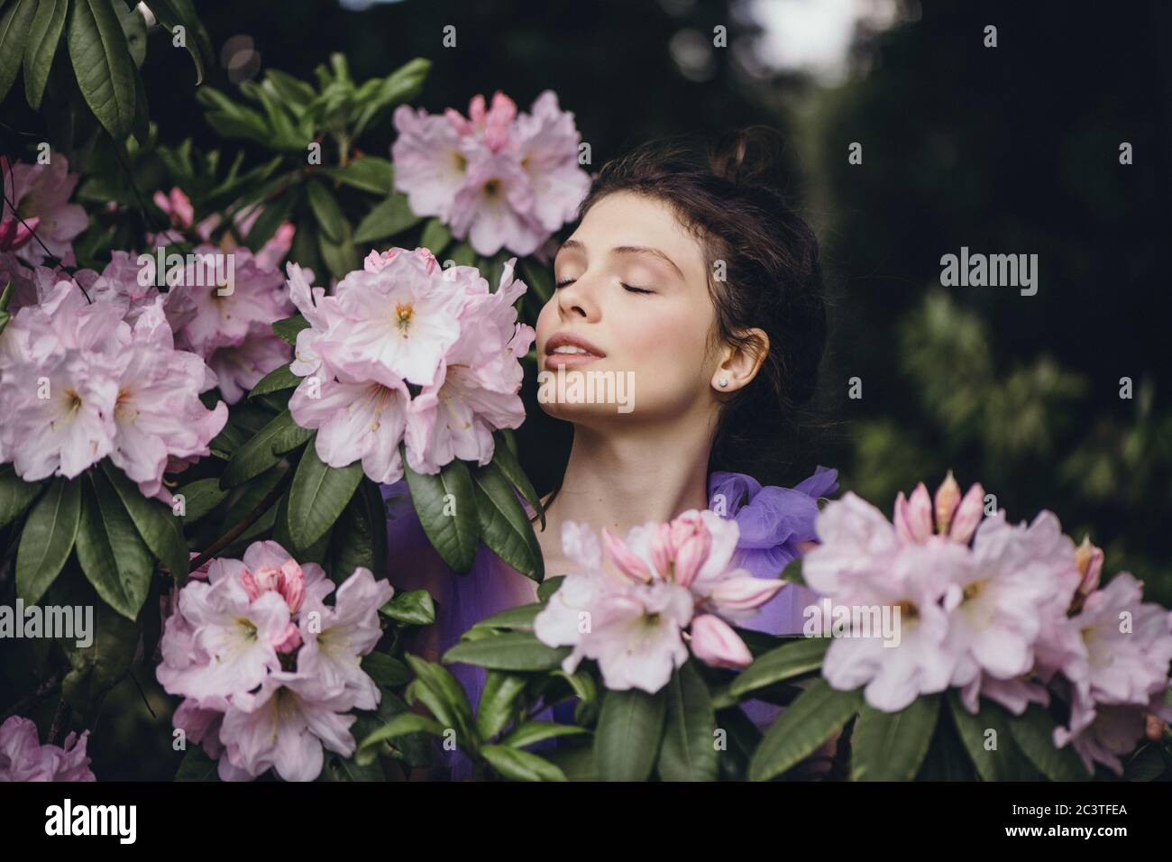 Porträt einer schönen jungen Frau mit geschlossenen Augen in blühenden Rhododendron Busch. Stockfoto