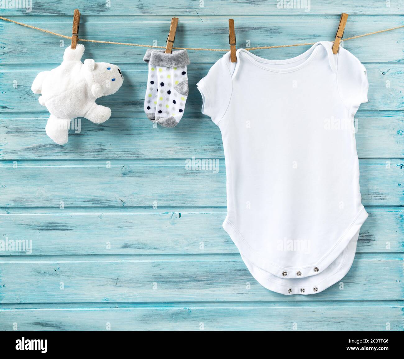 Baby Junge weiße Kleidung, weißes Bärenspielzeug und kleine Socken auf einer Wäscheleine, blauer Holzhintergrund Stockfoto