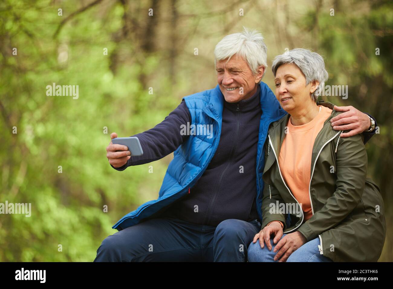 Portrait eines aktiven älteren Paares, das Selfie-Foto über Smartphone macht, während er sich während der Wanderung im Herbstwald ausruhte, Platz kopieren Stockfoto