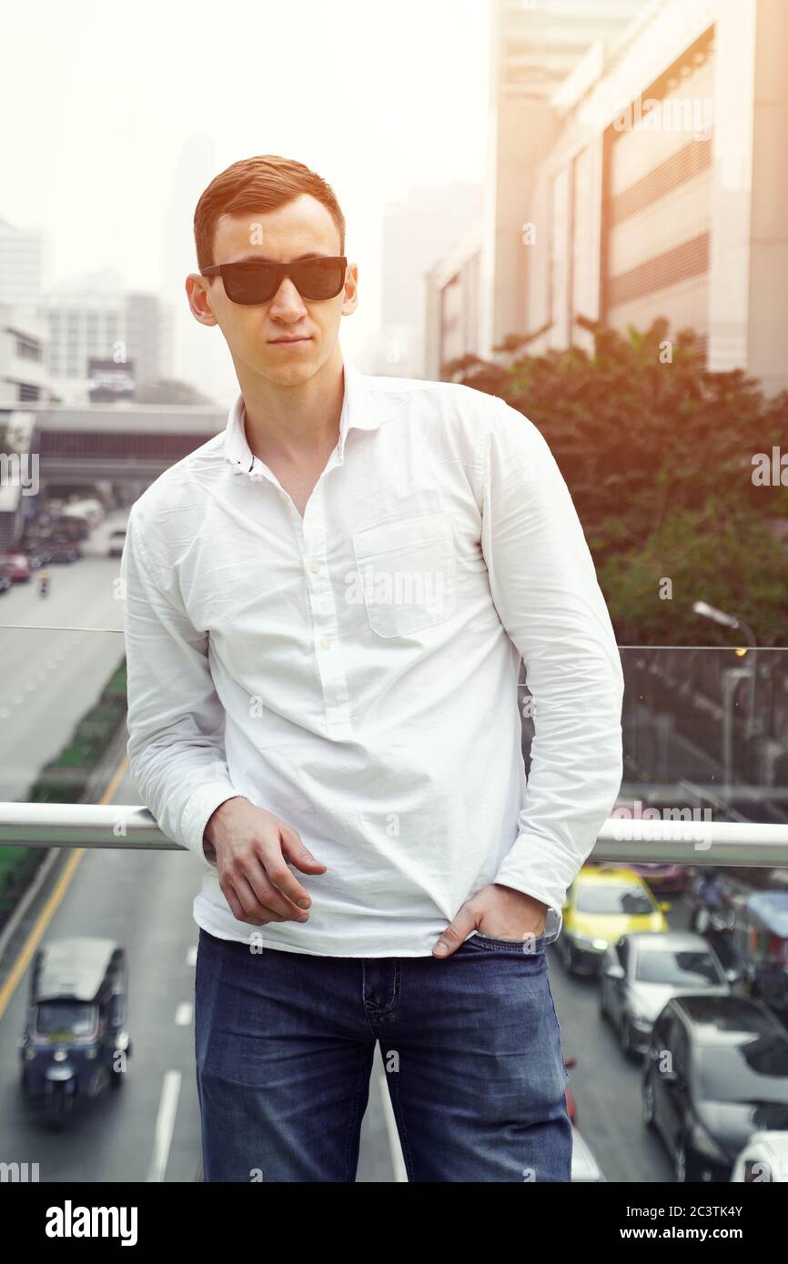 Schöner Mann in Sonnenbrille und einem weißen Hemd auf einer Brücke auf dem Hintergrund der Straße. Stockfoto