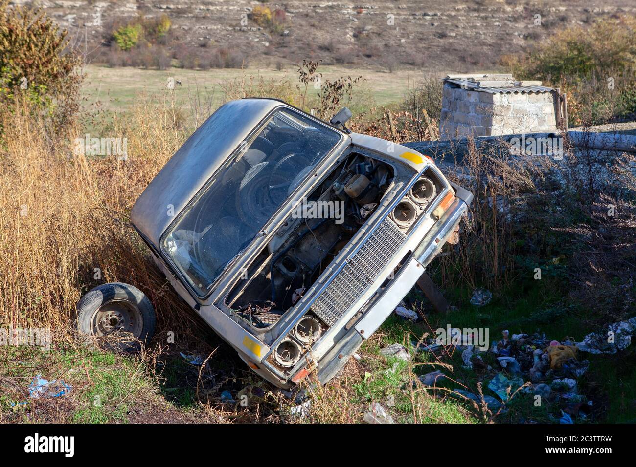 Altes Auto wird in den Müll geworfen. Verlassene Automobil am Müllcontainer Stockfoto