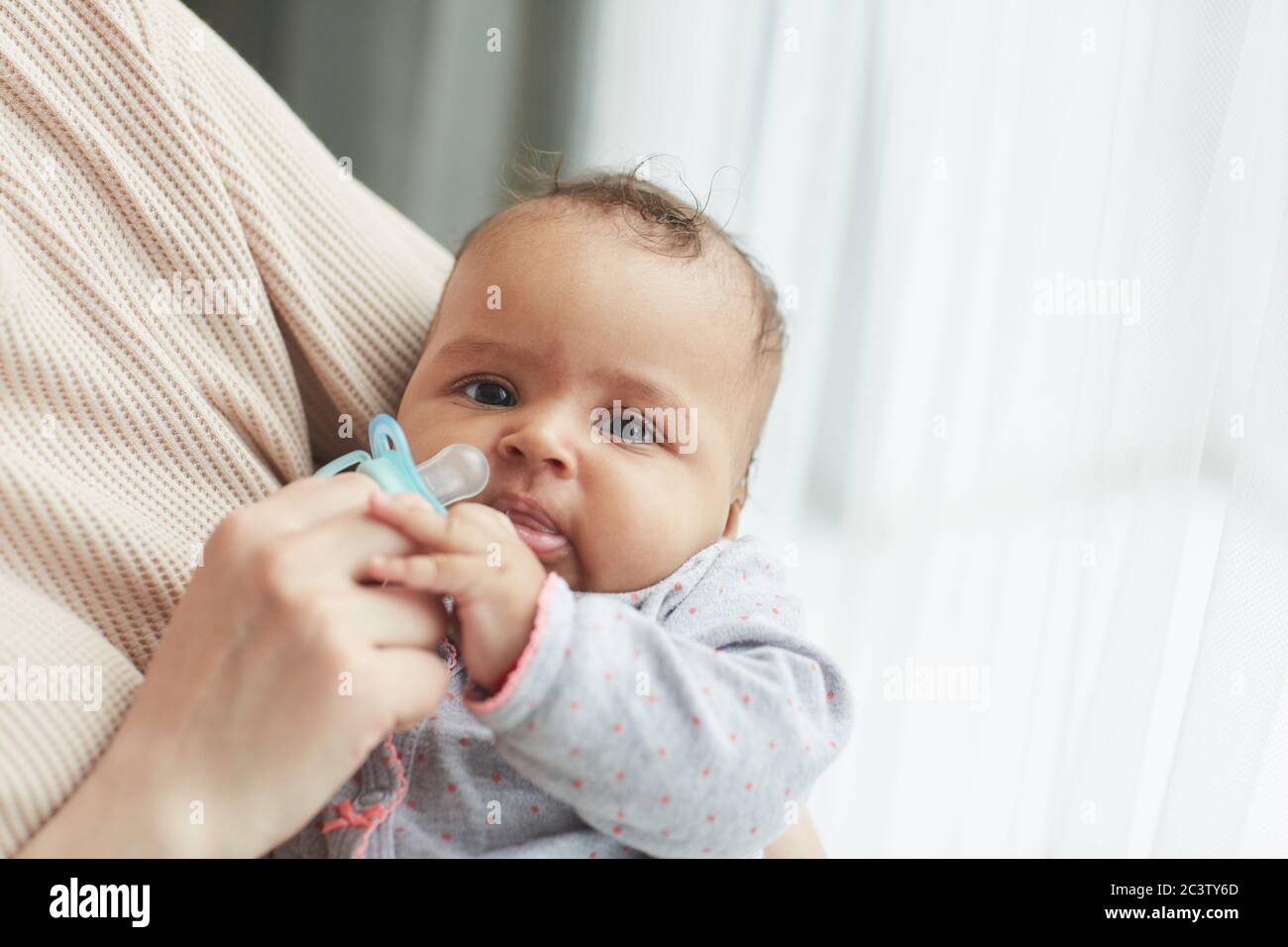 Nahaufnahme Porträt von niedlichen gemischt Rennen Baby Blick auf Kamera, während in Mutter Arme am Fenster zu Hause, kopieren Raum Stockfoto