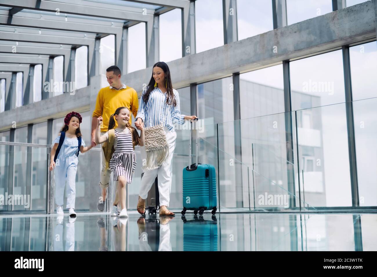 Familie mit zwei Kindern, die in den Urlaub fahren, am Flughafen mit Gepäck spazieren gehen. Stockfoto