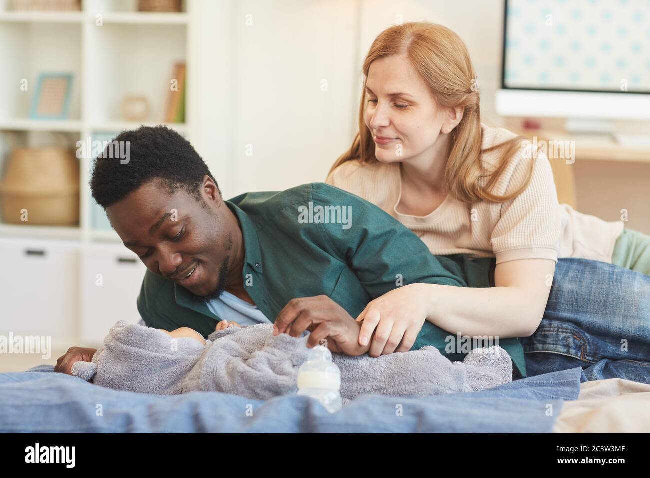 Portrait von glücklichen interracial Familie spielen mit Baby Junge, während auf dem Bett in gemütlichen Zuhause Interieur, kopieren Raum liegen Stockfoto