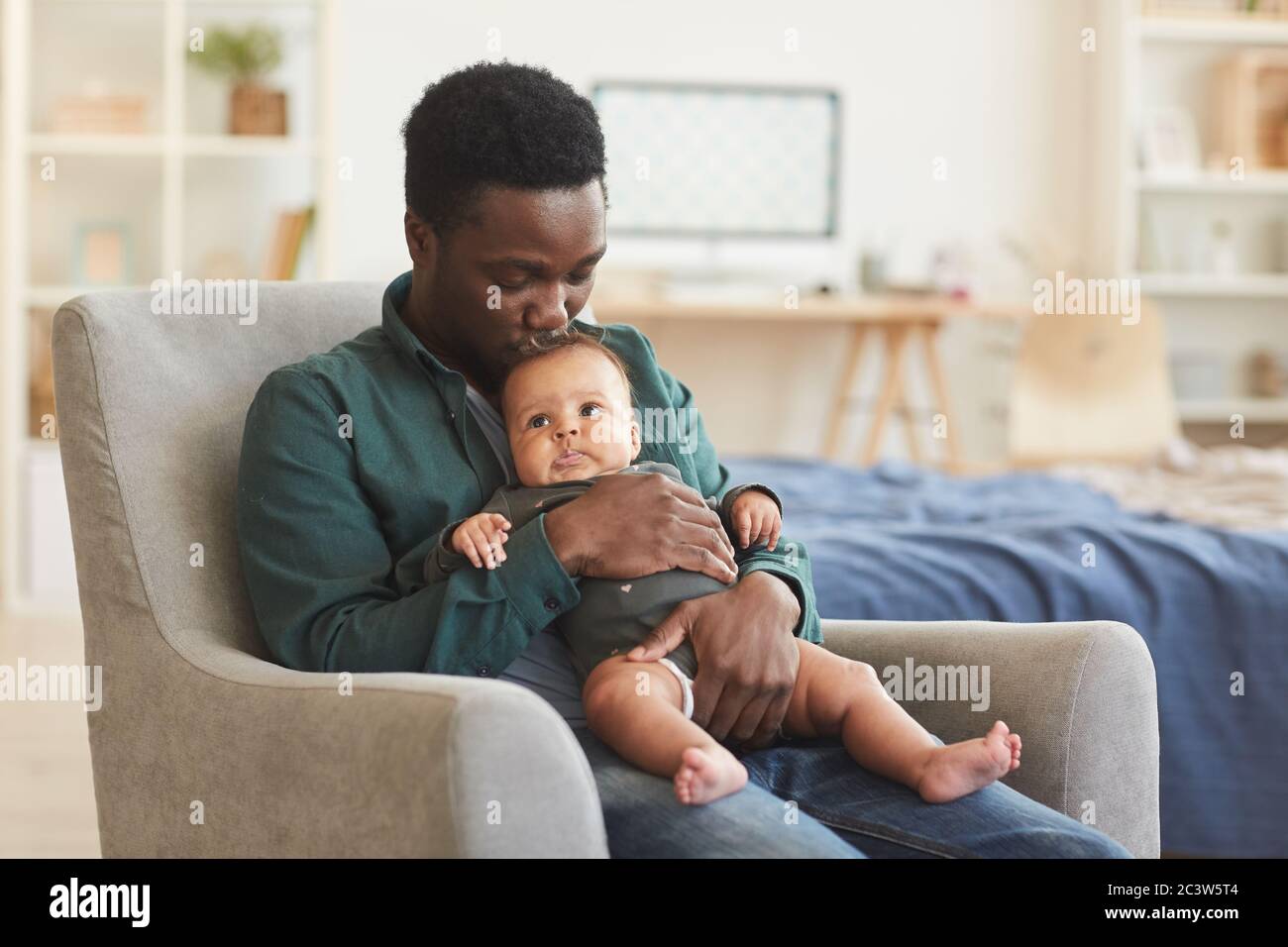 Porträt von fürsorglichem afroamerikanischen Mann hält niedlichen Mixed-Race Baby, während in bequemen Sessel zu Hause sitzen, kopieren Raum Stockfoto