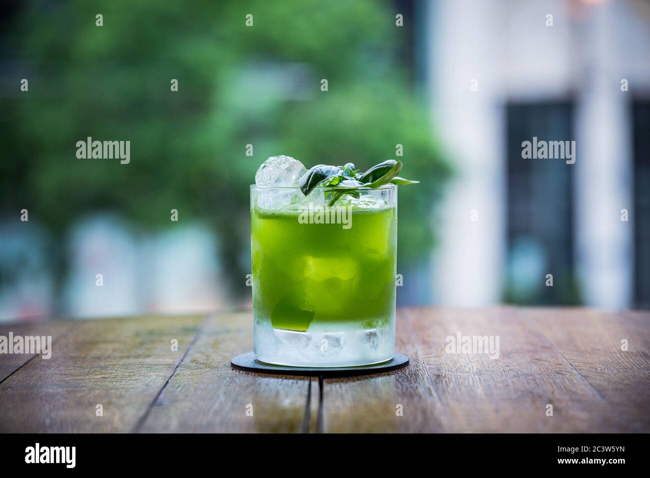 Man kann einen Cocktail namens Gin Basilikum Smash auf einem Tisch sehen, dessen grüne Farbe stark ist und einen verschwommenen Hintergrund hat Stockfoto