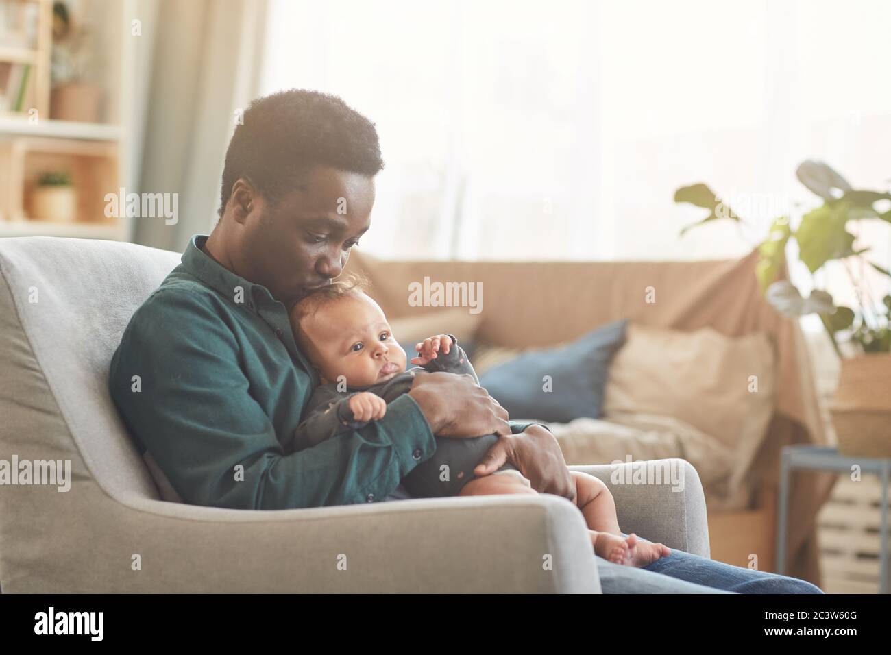 Seitenansicht Porträt von fürsorglichen afroamerikanischen Mann hält niedlichen Mixed-Race Baby, während sitzen in bequemen Sessel zu Hause, kopieren Raum Stockfoto