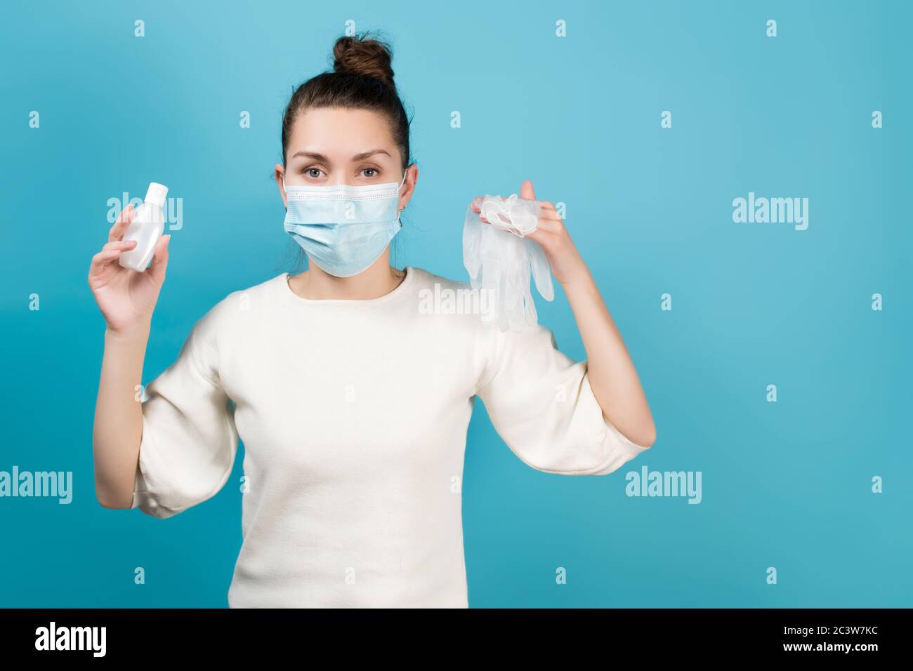 Junge Frau Sanitäter in einer medizinischen Maske hält in ihr Hände ein Desinfektionsmittel in einem Behälter und medizinische Handschuhe Stockfoto