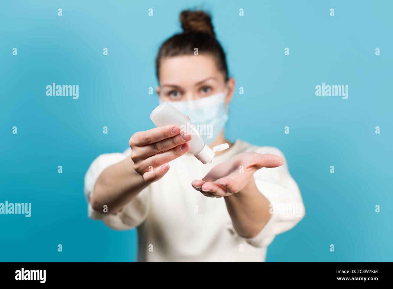 Weibchen in einer medizinischen Maske drückt ein Desinfektionsmittel in die Handfläche ihrer Hand Stockfoto