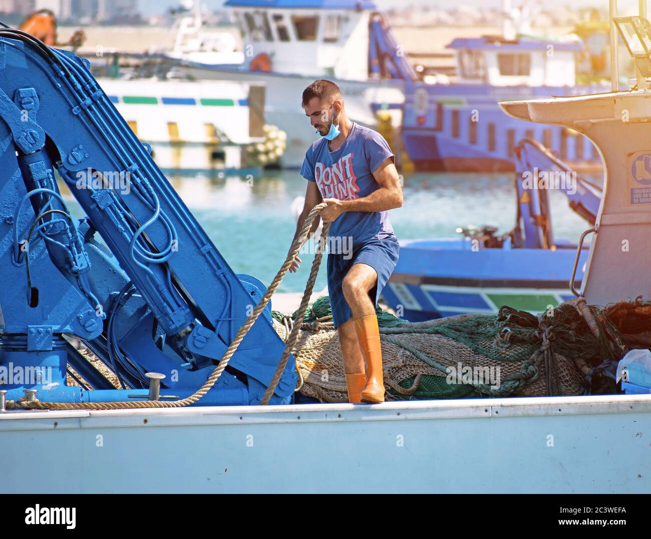 San Pedro del Pinatar, Murcia, Spanien, 22. Juni 2020: Ein Besatzungsmitarbeiter an Bord eines Fischerbootes oder Schiffes, der die Seile für den Hafen vorbereitet Stockfoto