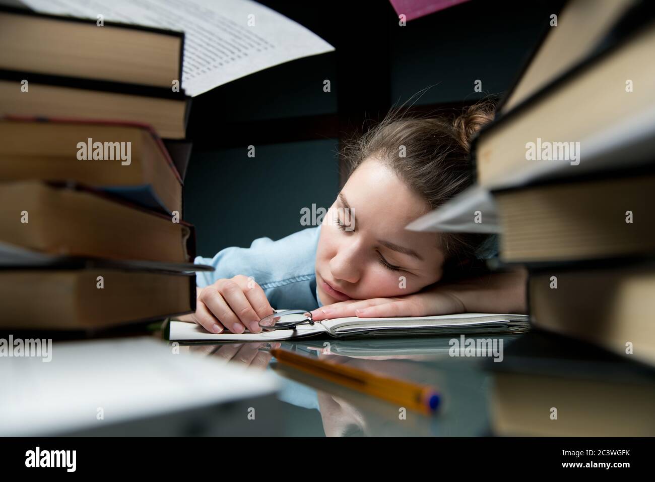 Eine junge Frau schläft an einem Tisch, der mit Büchern und Notizbüchern übersät ist. Stockfoto