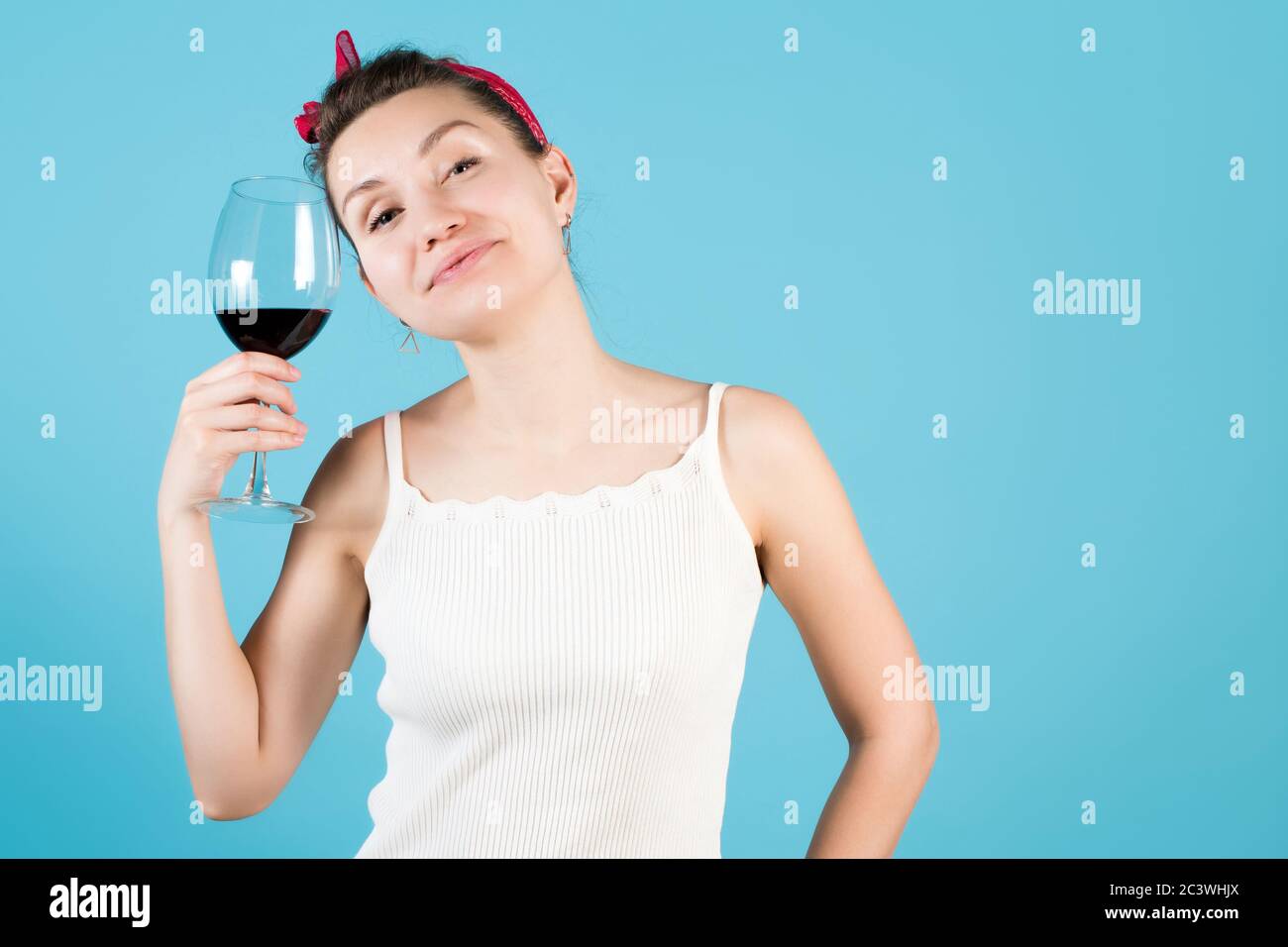 Nahaufnahme einer jungen Frau auf blauem Hintergrund, hält sie ein Glas mit Rotwein Stockfoto