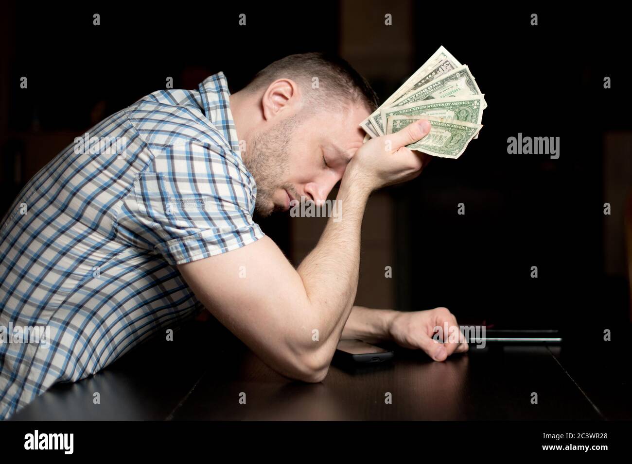 Verärgert Mann hält bescheidene Dollar-Einsparungen sitzen an einem Tisch Spät in die Nacht Stockfoto