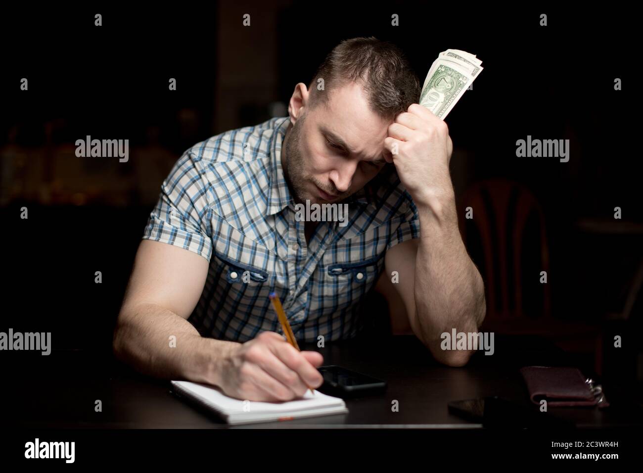 Der Mensch hält eine bescheidene Menge Geld und macht Notizen In einem Notizbuch Stockfoto