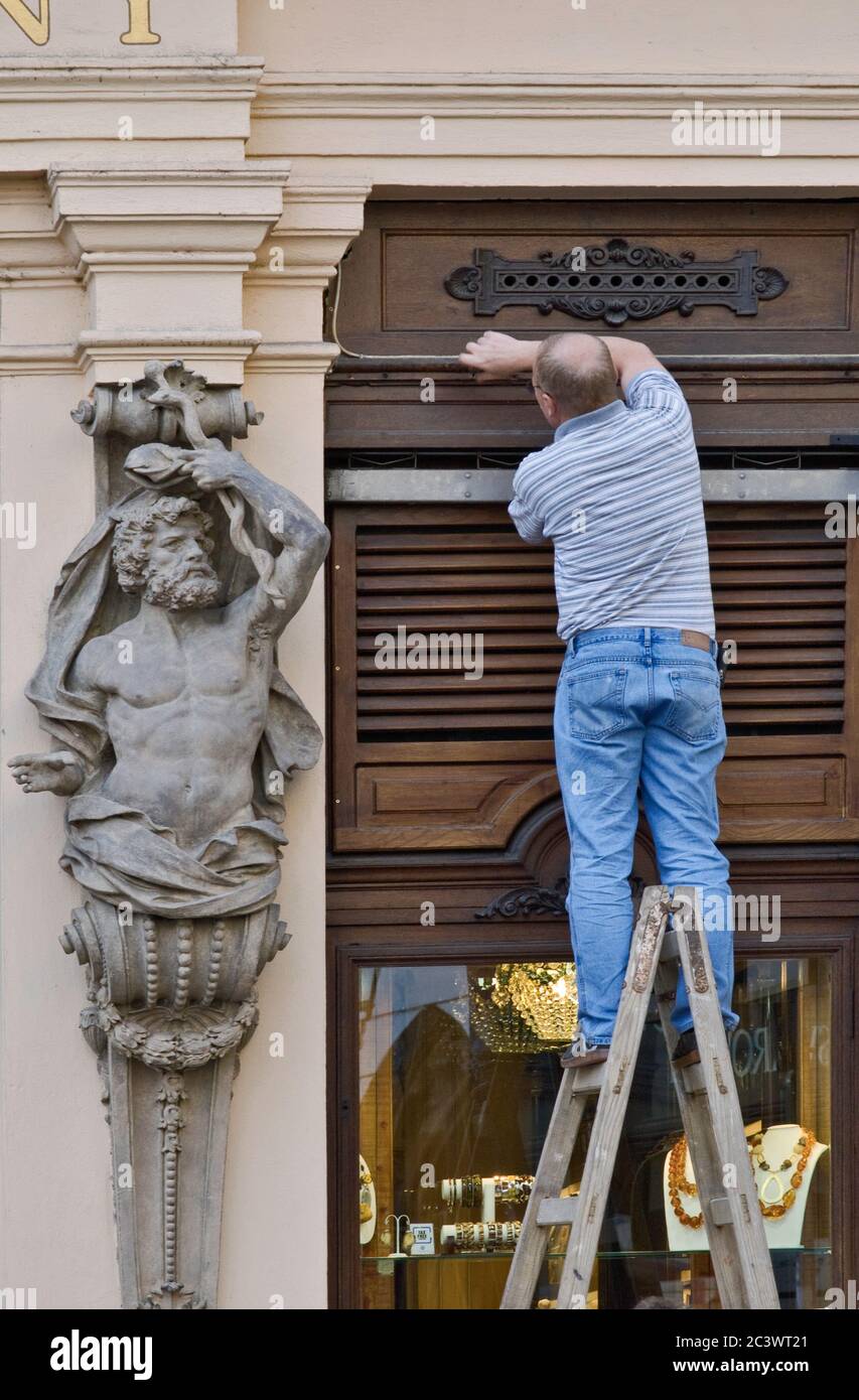 Reparaturmann und eine atlant-Skulptur am Eingang zum „at Golden Crown“-Geschäft im Male Namesti in der Altstadt, Prag, Tschechische Republik Stockfoto