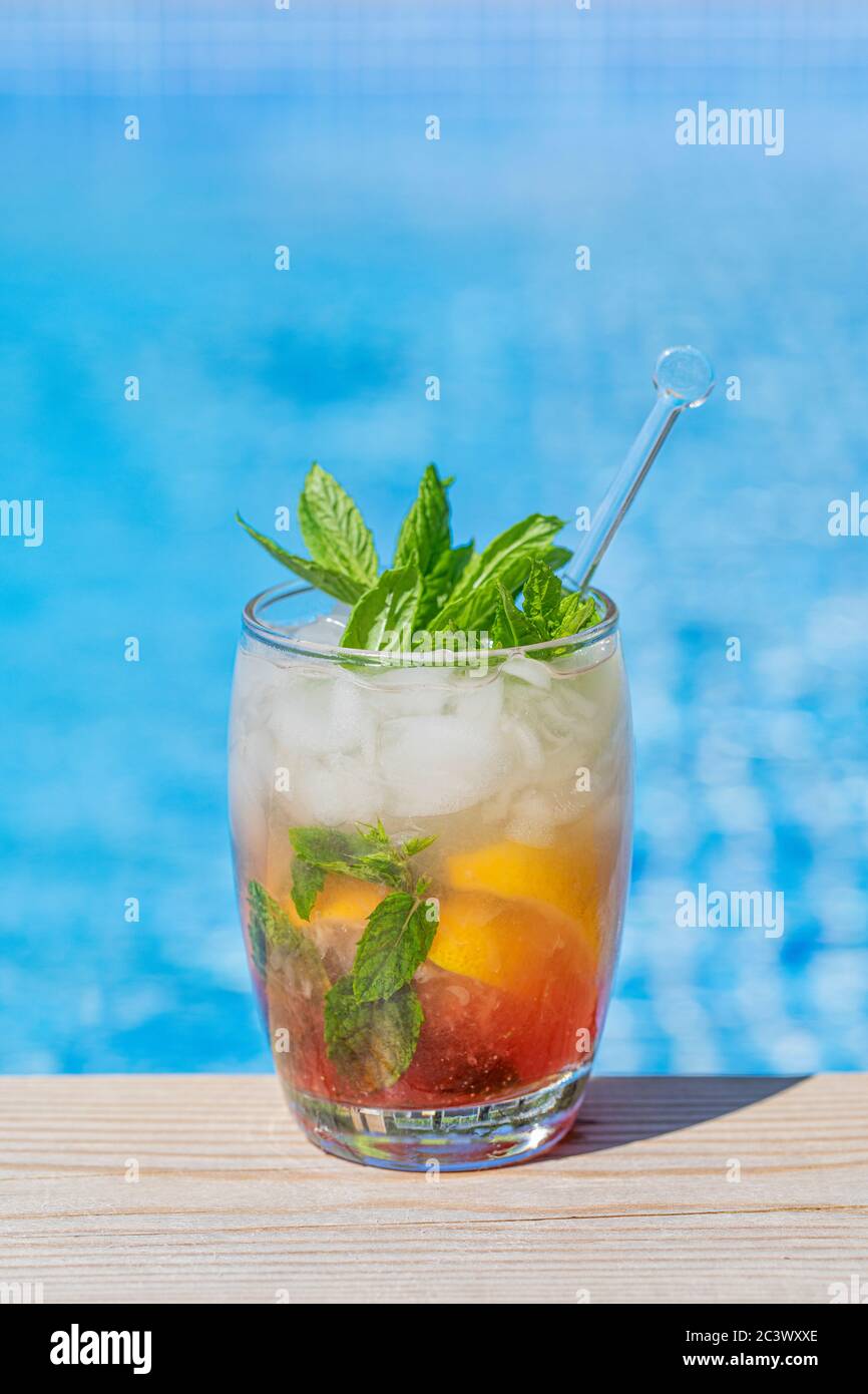 Ein frischer Sommerdrink am Pool. Das Getränk mit Minzblättern und Zitronenscheiben ist am Boden rot, und es hat mit zerkleinertem Eis und frischen Minzblättern Stockfoto