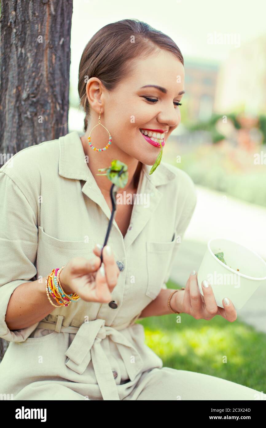 Glückliche positive Frau essen Salat im Park im Sommer Stockfoto